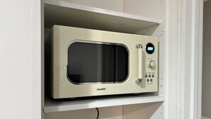 A microwave oven on a white shelf with a power cord plugged in.