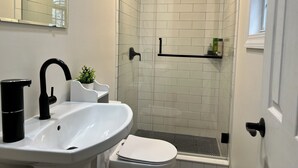 A bathroom with a white sink, black faucet, white toilet, and a glass shower enclosure.