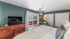 Un dormitorio con una cama, televisor, cómoda, ventilador de techo y puerta corrediza que da a un área exterior.