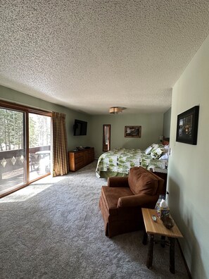 A bedroom with a bed, a chair, a small table, and a window with curtains.