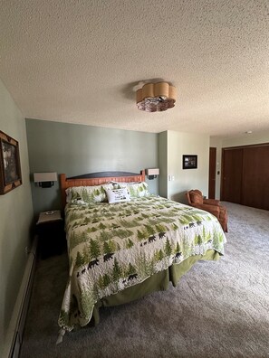 A bedroom with a bed, a nightstand, a lamp, a chair, and a door.