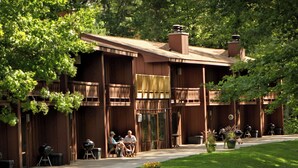 A wooden lodge with outdoor seating, a covered patio, and a well-maintained lawn.
