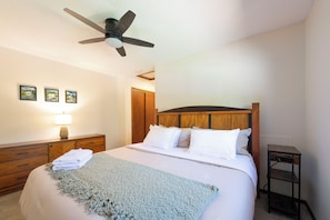 A bedroom with a bed, a ceiling fan, a bedside table, and a nightstand.