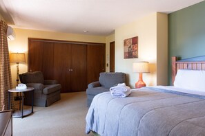 Ein Hotelzimmer mit einem Bett, zwei Sesseln, einem kleinen Tisch, einer Lampe und einer Tür.