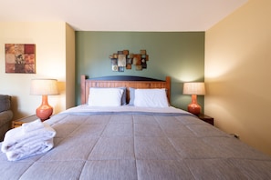 Une chambre d’hôtel avec un lit, deux tables de chevet avec des lampes, une œuvre d’art accrochée au mur au-dessus du lit, et une serviette pliée posée sur le lit.