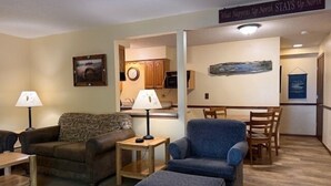 Una sala de estar con sofá, sillón y reposapiés, un comedor con mesa y sillas, y una cocina al fondo.
