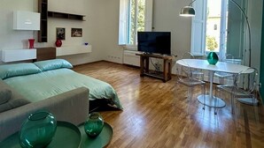 Moderni olohuone, jossa on sohva, televisio, ruokapöytä tuoleineen ja kattovalaisin.