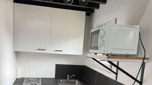 Une cuisine compacte équipée d’un lave-linge, d’un four à micro-ondes et d’une petite table en bois.