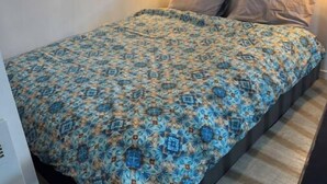 Une petite chambre avec un lit simple, une couvre-lit à motifs, une lampe fixée au mur et une fenêtre avec un miroir.