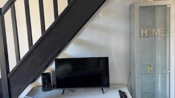 Un escalier avec des rampes noires, un meuble de rangement blanc intégrant un téléviseur à écran plat, et une vitrine sur laquelle est inscrit le mot « MAISON ».