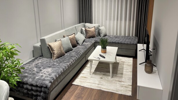 Una sala de estar moderna con un sofá seccional gris, una mesita de centro blanca y una planta en maceta.