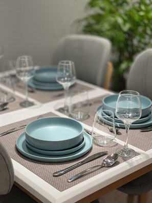 A dining table set with blue plates, clear glasses, and silverware, with a plant in the background. - Comfort Inn Hotel (Kukës)