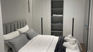 Un dormitorio moderno con cama, ropa de cama gris y blanca, un plaid oscuro y un armario empotrado con estantes.
