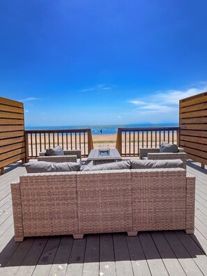 A wooden deck with a wicker sofa and a table, overlooking a beach. - NEW! The Shipwreck Studio (Corpus Christi)
