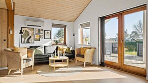 A spacious living room with a large sliding glass door leading to a patio, a black leather sofa, wicker chairs, and a coffee table.