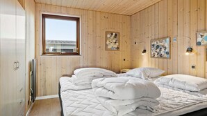 A wooden-paneled bedroom with a large window, two wall-mounted light fixtures, and a bed with white bedding.