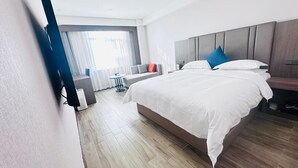 Ein modernes Hotelzimmer mit einem großen Bett, einer Couch, einem kleinen Tisch und Blick ins Freie.