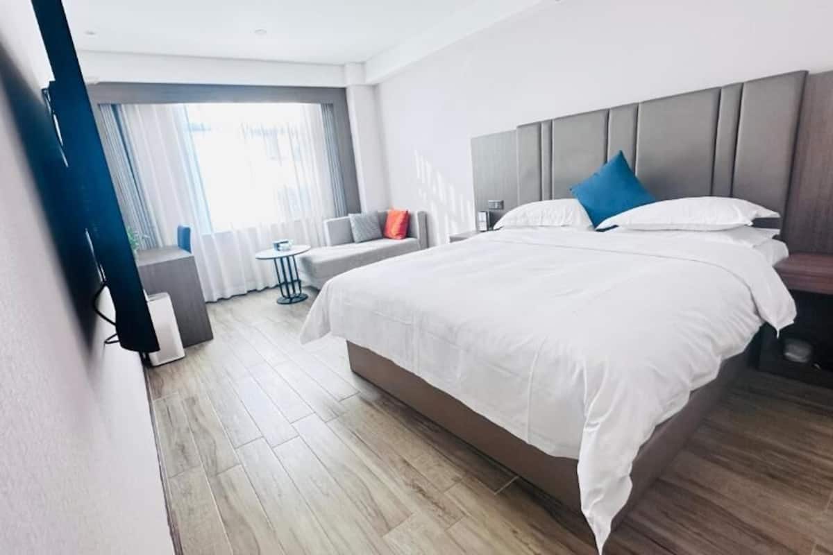 A modern hotel room with a large bed, a sofa, a small table, and a view of the outdoors.