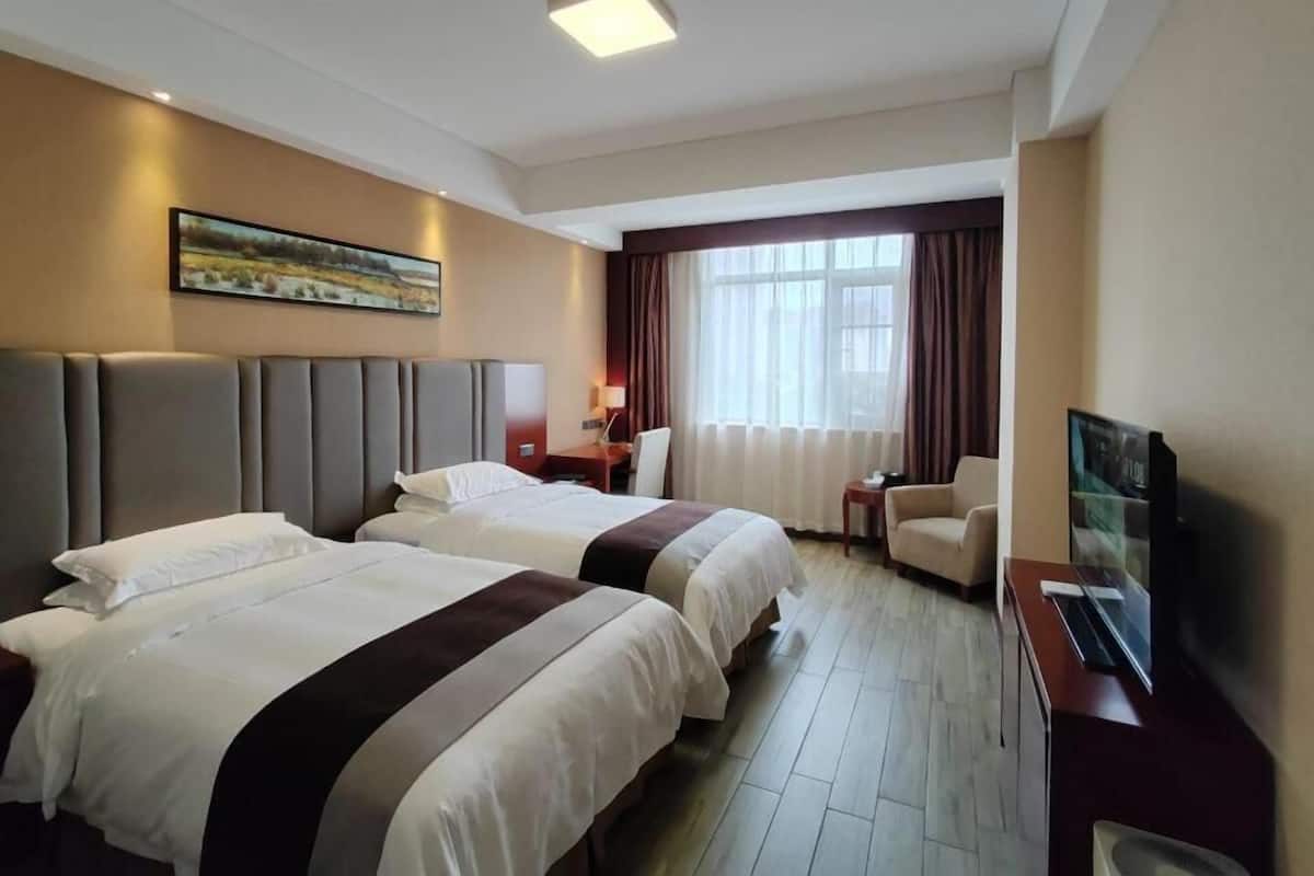 A hotel room with two beds, a desk, a chair, a TV, and a window with curtains.