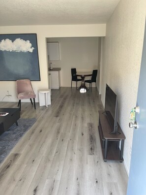 En moderne stue med spiseplads, et stort maleri, en lyserød stol, et lille bord og et fjernsyn.