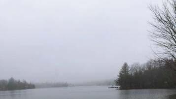 Un lac avec une jetée en bois et une plage de sable, entouré d’arbres et surplombé d’un ciel nuageux.