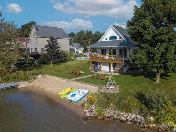 A lakeside property with a house featuring a balcony, a dock, and a sandy beach area. - Lakefront | 2 Saunas, Firepit, Kayaks, Dock & Boat (Lake)