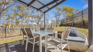 An outdoor patio with a glass table and chairs, surrounded by a wooden fence and trees. - NorthStar 5 (Jindabyne)