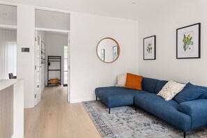 A modern living room with a blue sofa, a round mirror, and two framed botanical illustrations.