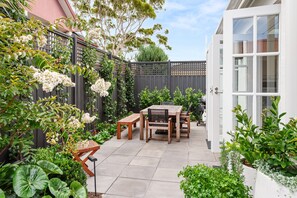 A patio with a wooden table and chairs, surrounded by lush greenery and flowering plants. - Hampton Beach Pearl Near Beach (Hampton)