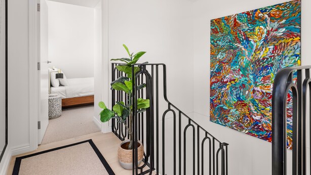 Een hal met een bed, een groot abstract schilderij en een plant in pot.