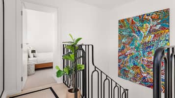 A hallway with a bed, a large abstract painting, and a potted plant.