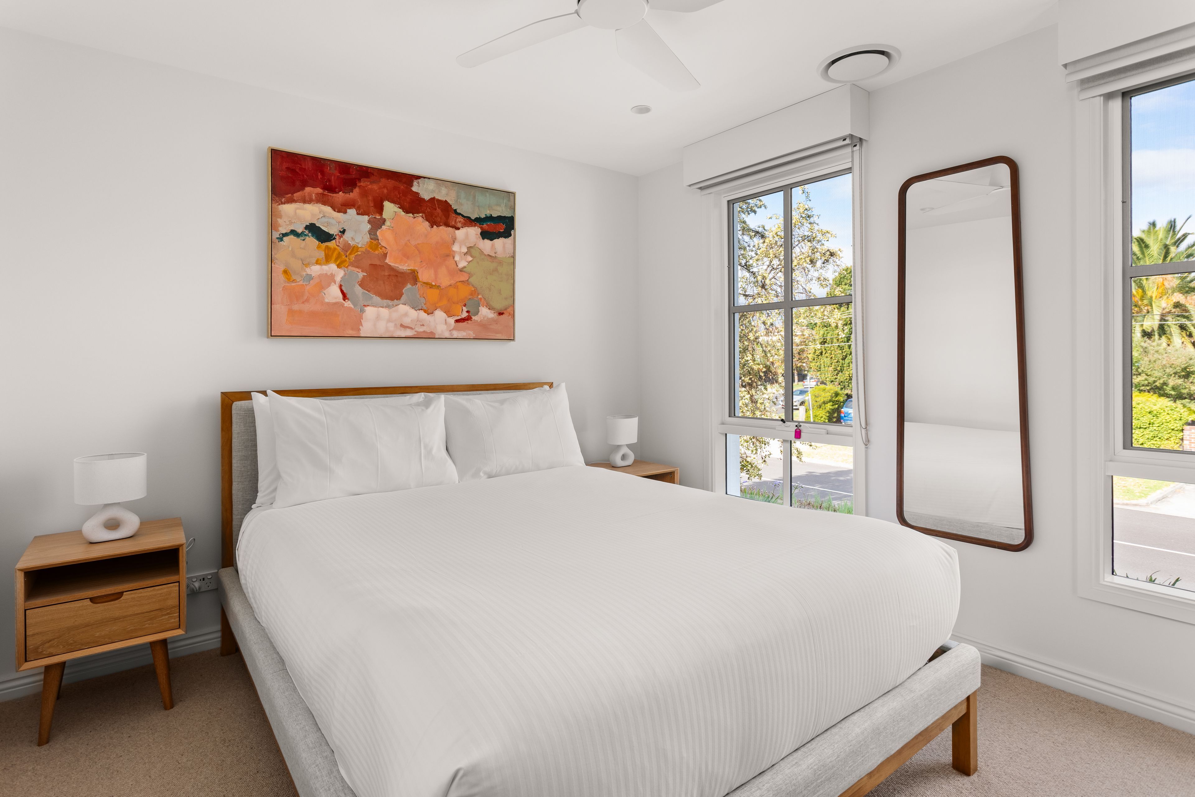 Une chambre à coucher avec un lit, une table de chevet, une lampe, un ventilateur de plafond, une fenêtre donnant sur un beau paysage et un tableau accroché au mur.