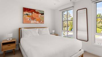Une chambre à coucher avec un lit, une table de chevet, une lampe, un ventilateur de plafond, une fenêtre donnant sur un beau paysage et un tableau accroché au mur.