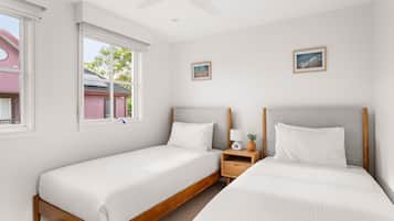 A hotel room with two single beds, a nightstand, a ceiling fan, and two framed pictures on the wall.