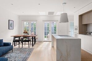 A modern kitchen with a marble island, wooden cabinets, and a dining area with a table and chairs. - Hampton Beach Pearl Near Beach (Hampton)