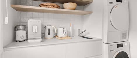 Una cocina moderna con lavadora integrada, cafetera, tostadora y hervidor.