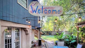 Eine Terrasse mit einem 'Welcome'-Schild, Sitzgelegenheiten im Freien und einem Garten im Hintergrund.