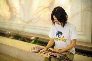 A person sitting on a bench with a book, in a setting with a marble wall and a decorative panel in the background. - Senlin Hotel (Guiyang)