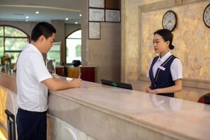 A reception area with a marble counter, framed certificates on the wall, and clocks. - Senlin Hotel (Guiyang)