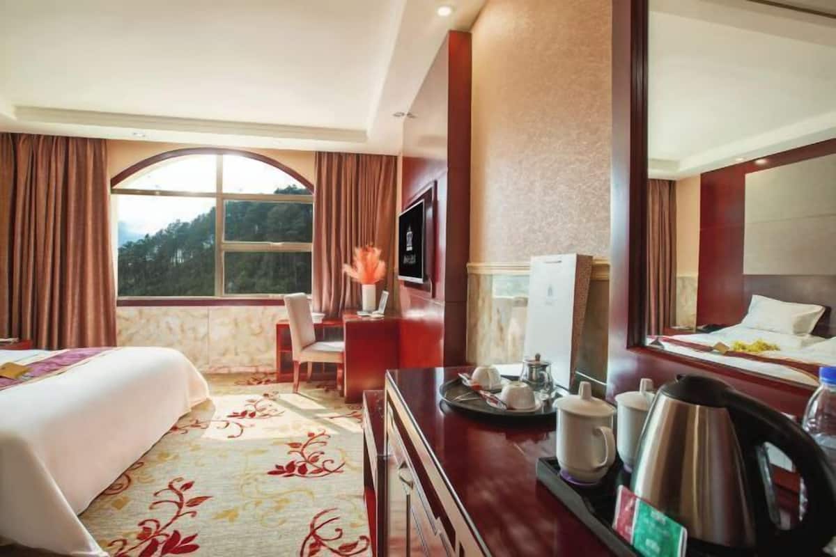 A hotel room with a bed, a desk with a chair, a television, and a breakfast tray with cups and a kettle.