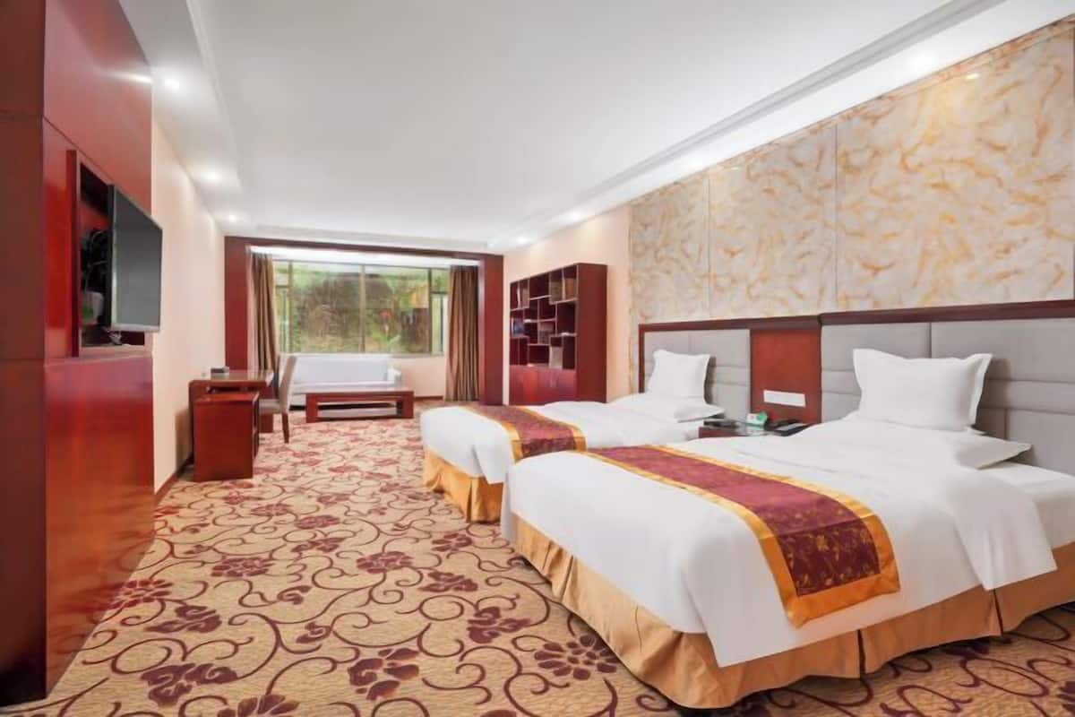 A hotel room with two beds, a desk, a chair, a TV, and a large window.