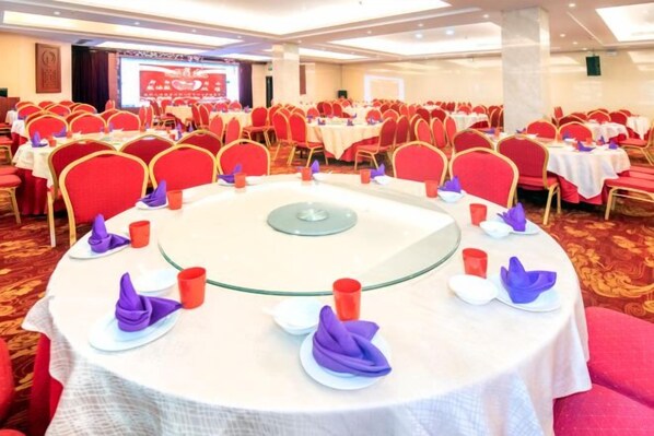 A conference room with round tables, red chairs, and white tablecloths.