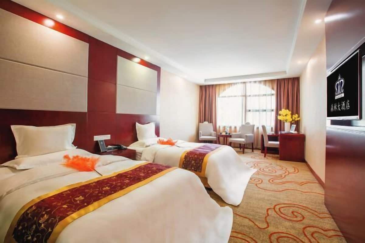 A hotel room with two beds, a desk, a chair, a TV, and a window with curtains.