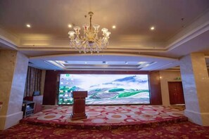 A hotel conference room with a large screen, a chandelier, and a patterned carpet.