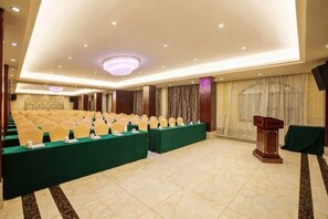 Un salón de conferencias con filas de sillas, un atril y suelo alfombrado.