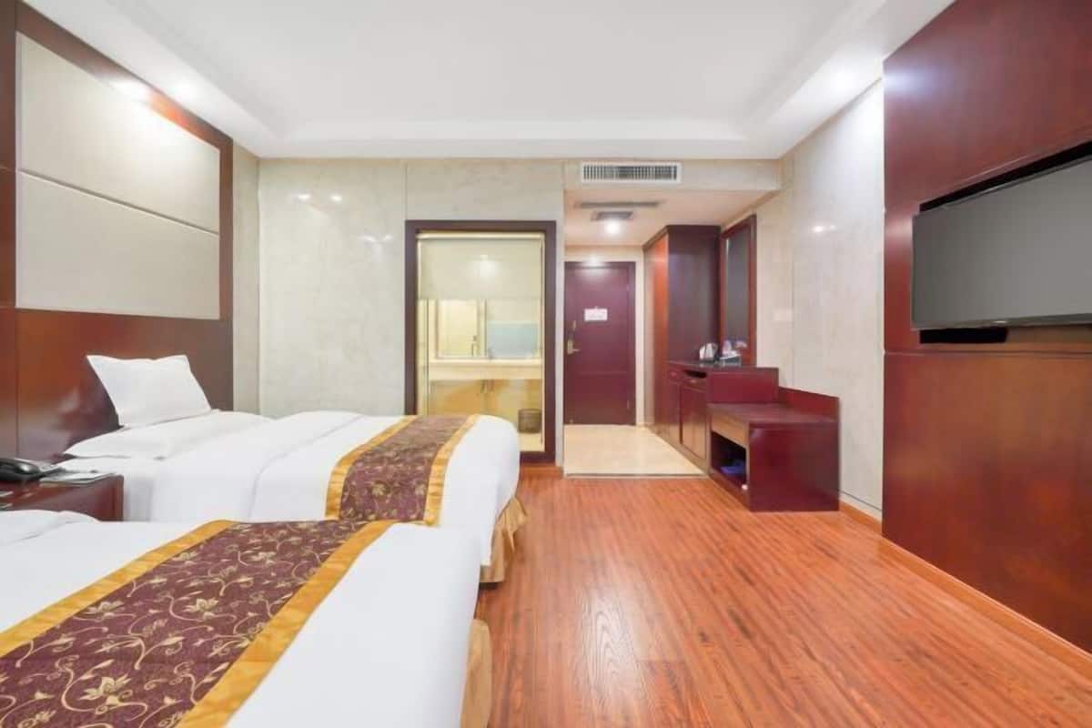 A hotel room with two beds, a TV, a bathroom, and a small sitting area.