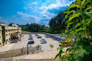 A parking lot with multiple cars, a building with a curved facade, and a mountainous backdrop. - Senlin Hotel (Guiyang)