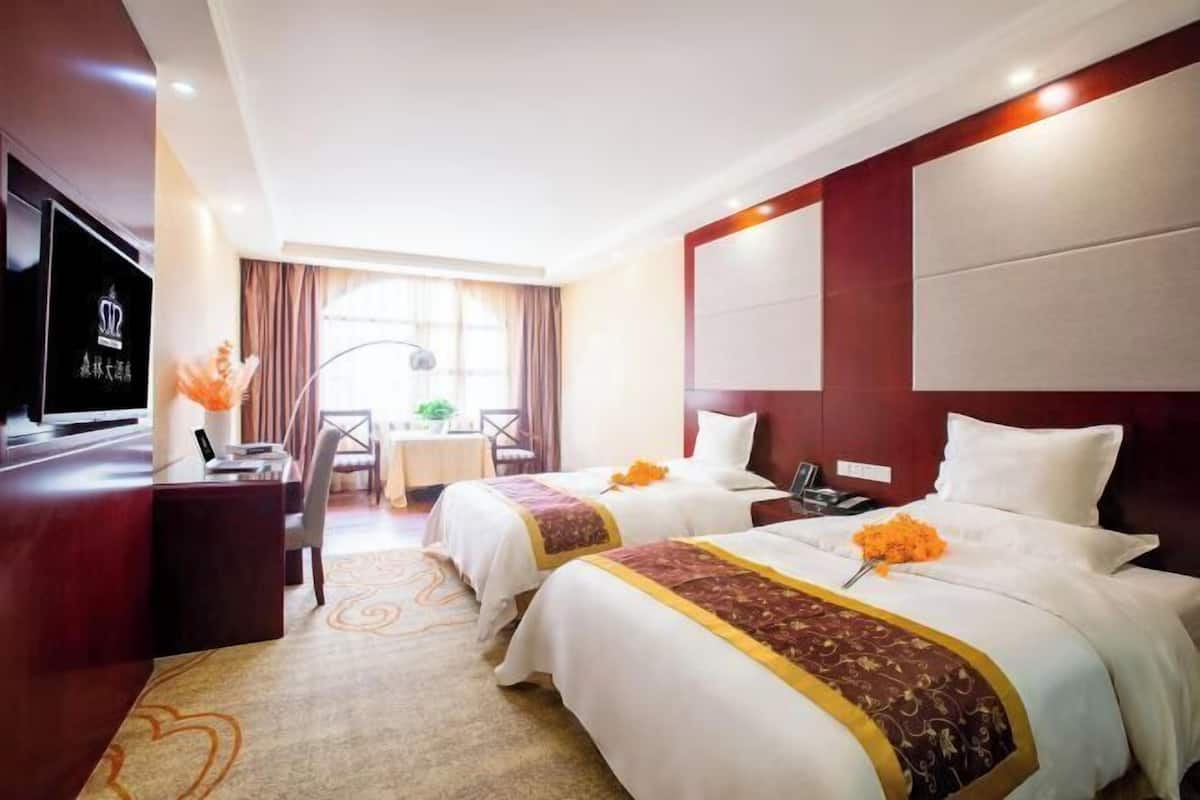 A hotel room with two beds, a desk, a TV, and a window with curtains.