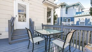 A deck with a glass table and four chairs, a wooden staircase, and a white door.