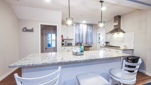 A modern kitchen with a granite island, white cabinetry, and pendant lighting.